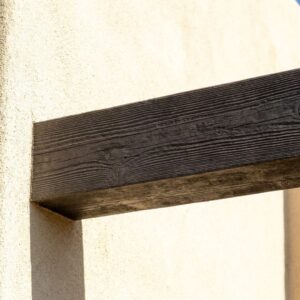 Detail shot of a perfectly straight faux wood beam installed against a sun-drenched stucco wall.